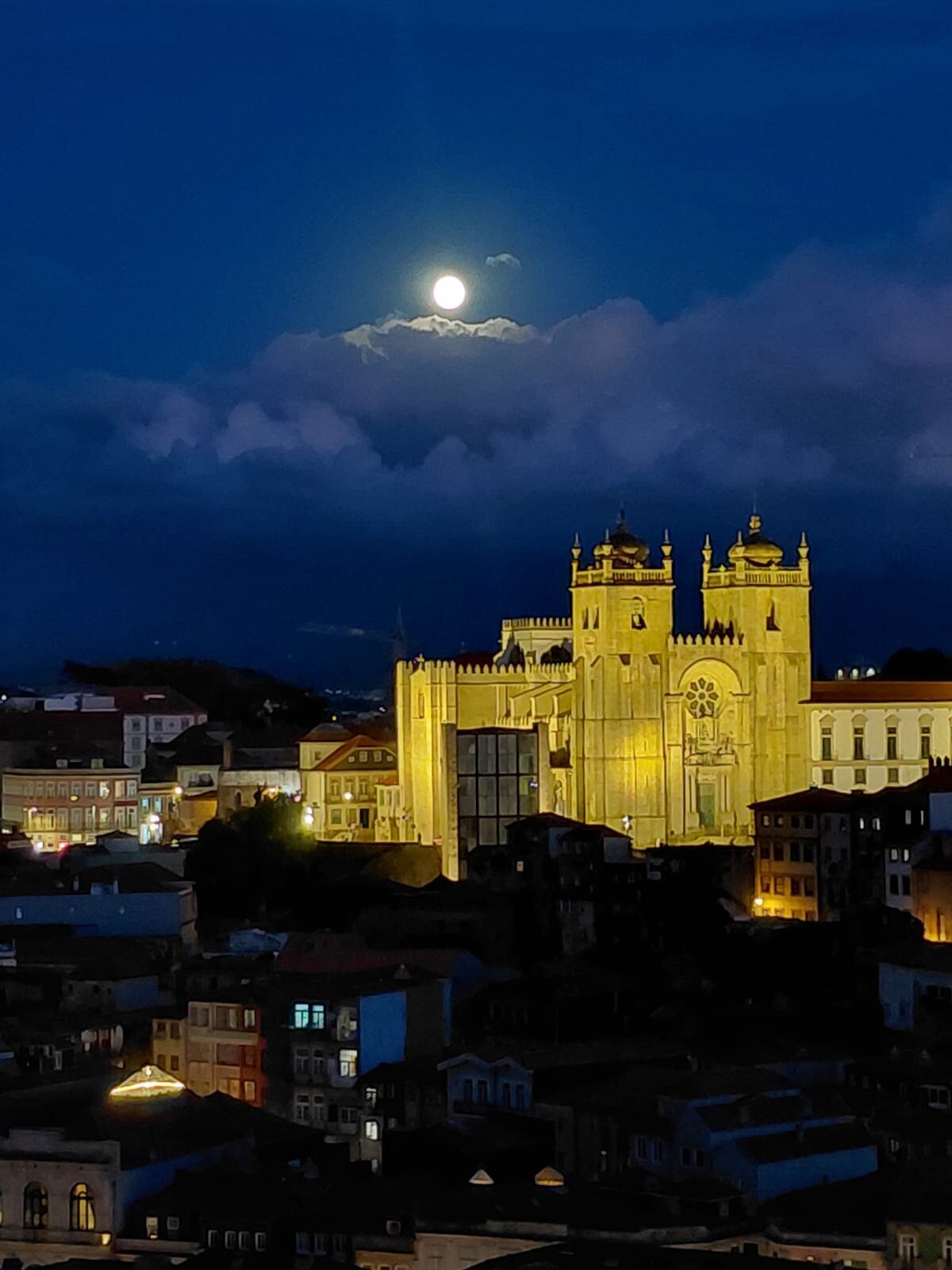 Full moon rising between clouds over Porto's illuminated Sé Cathedral, night view